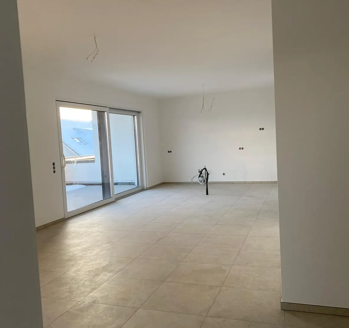 Raumgestaltung Objekt Aachen Dieses Bild zeigt einen hellen Raum mit beigen Fliesen und weißen Wänden. An der linken Seite des Bilde befindet sich eine Schiebetür als Ausgang auf die Dachterasse.